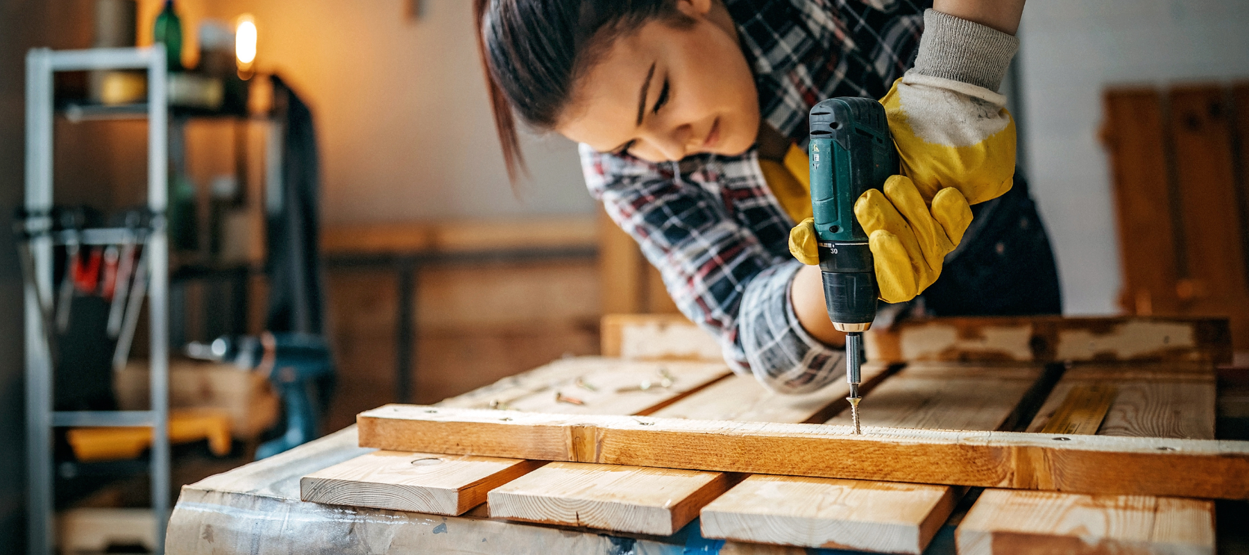 A woman using a power drill on a piece of lumber.